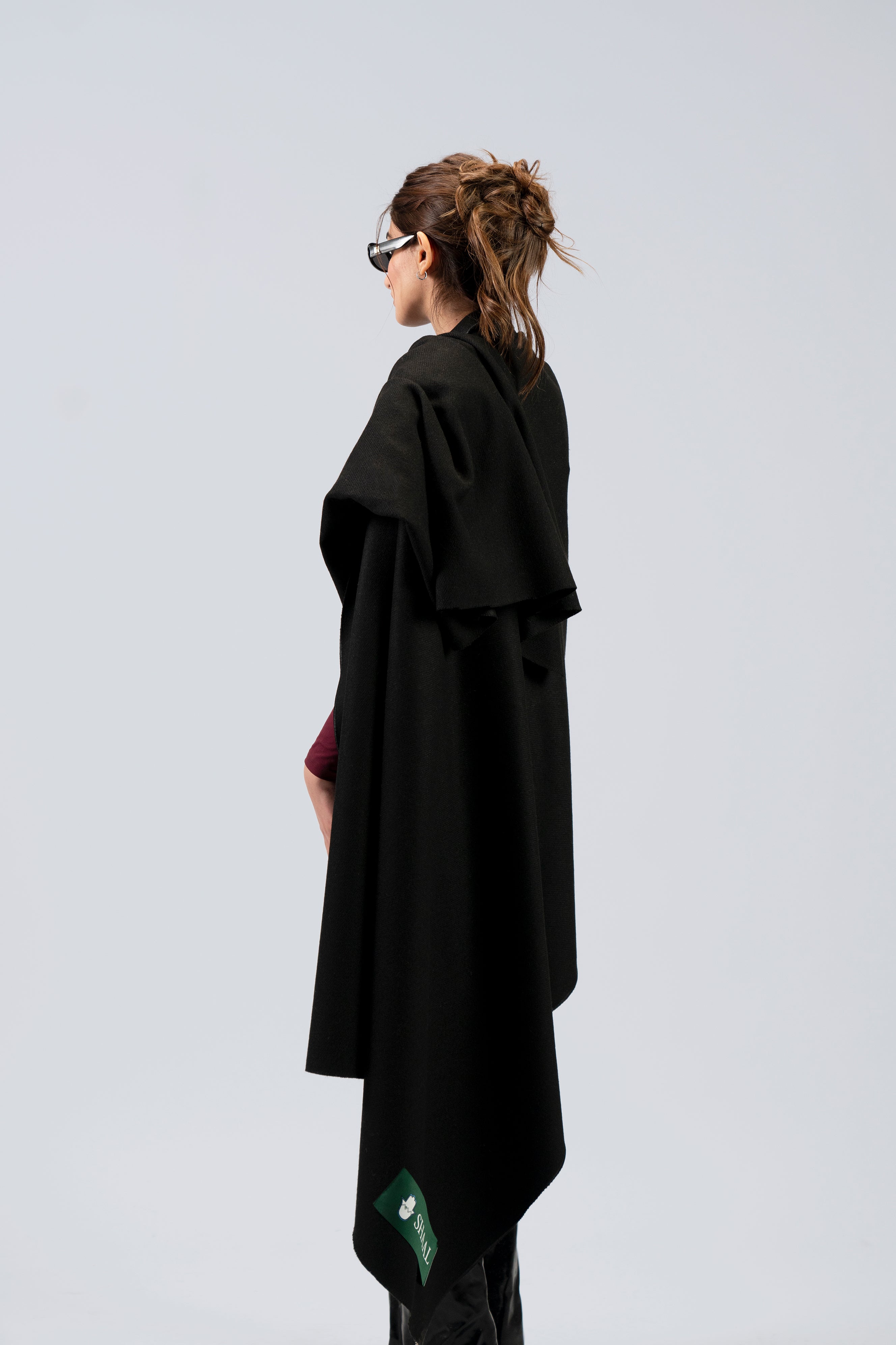 Black heavyweight lamb wool shawl wrapped around female model with sunglasses, three-quarter back view