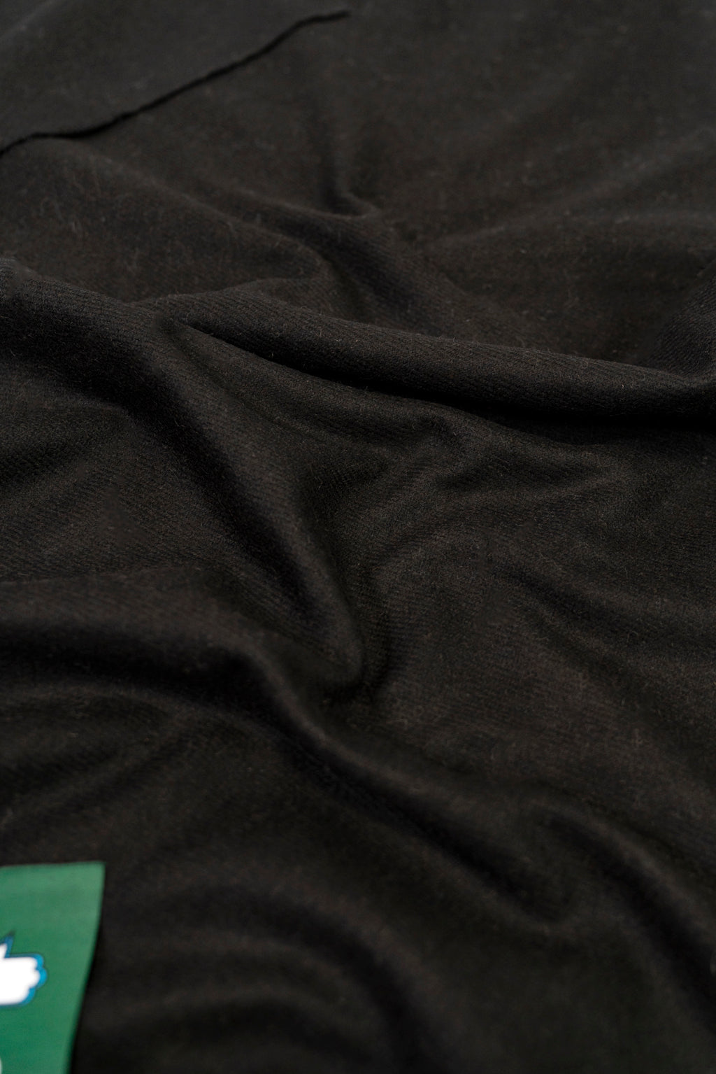 Black heavyweight lamb wool shawl close-up of soft fabric weave with green label corner