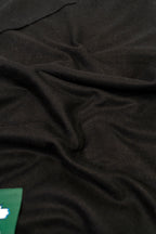 Black heavyweight lamb wool shawl close-up of soft fabric weave with green label corner