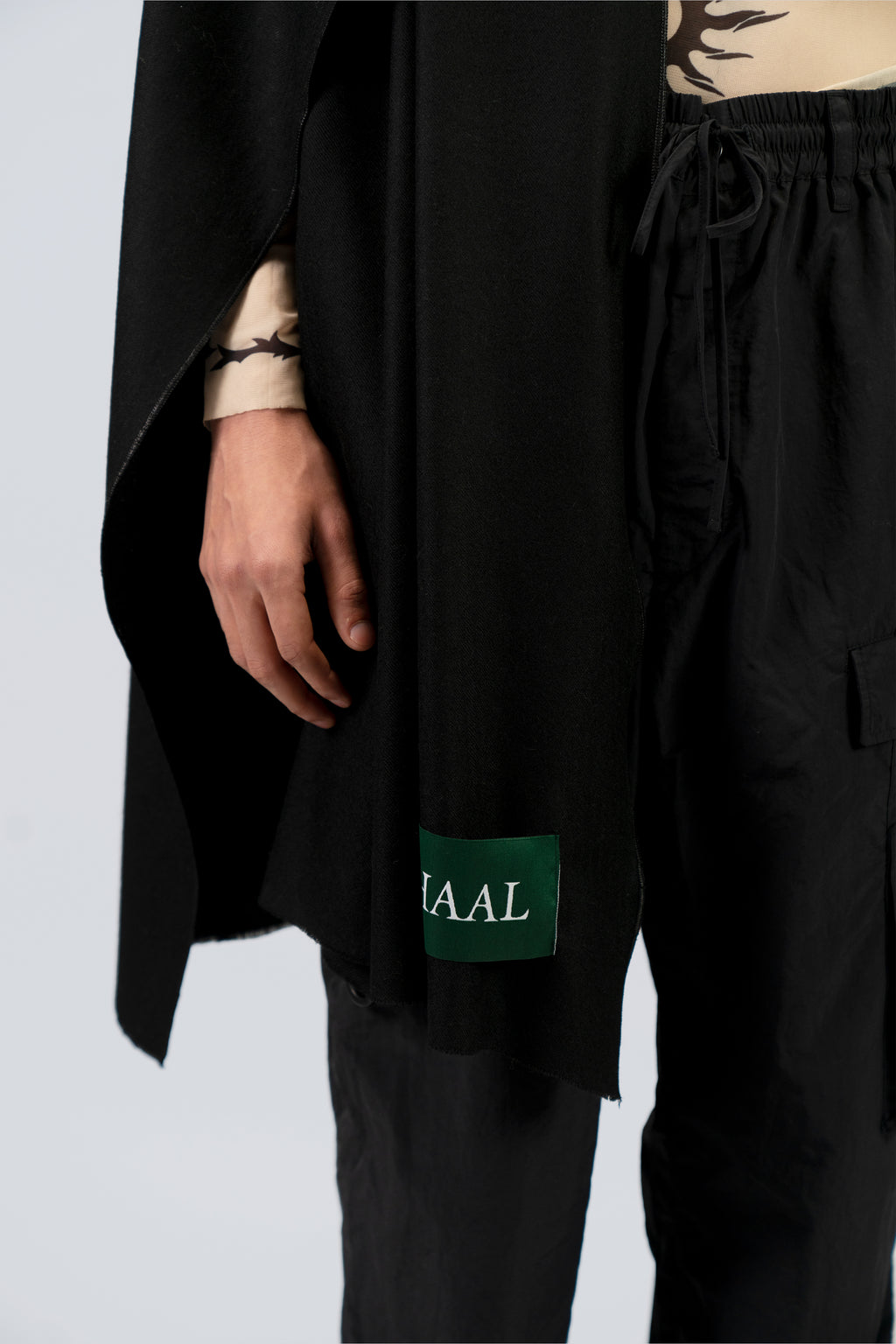 Black heavyweight lamb wool shawl with SHAAL label drape detail, male model mid-body view