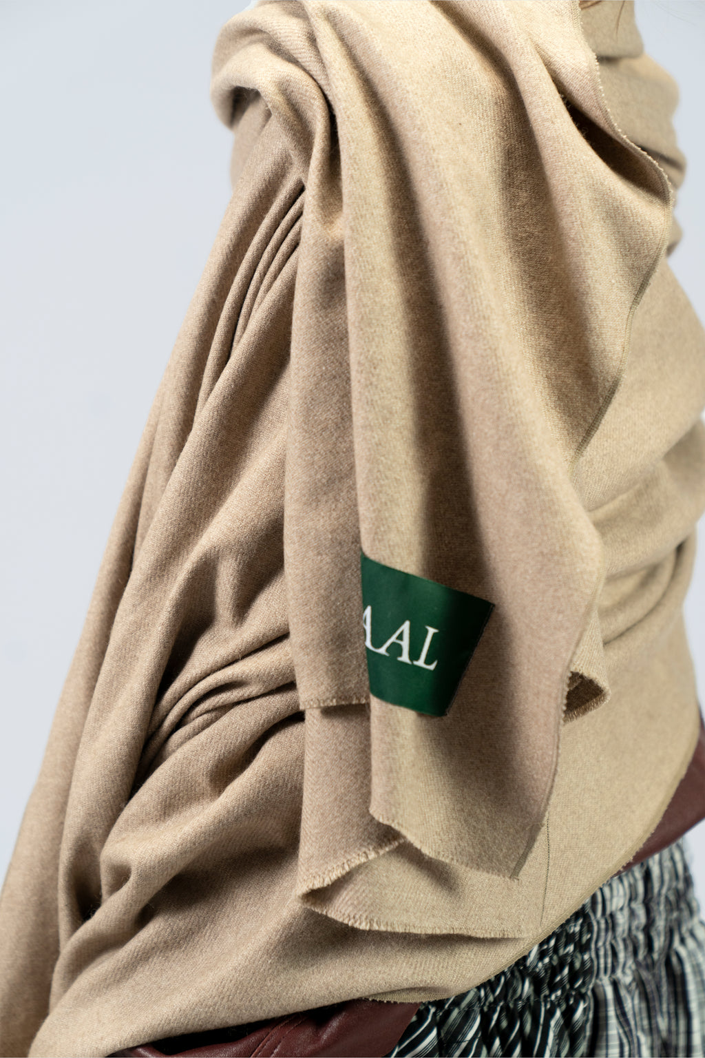 Beige heavyweight lamb wool shawl drape detail with SHAAL label over leather jacket