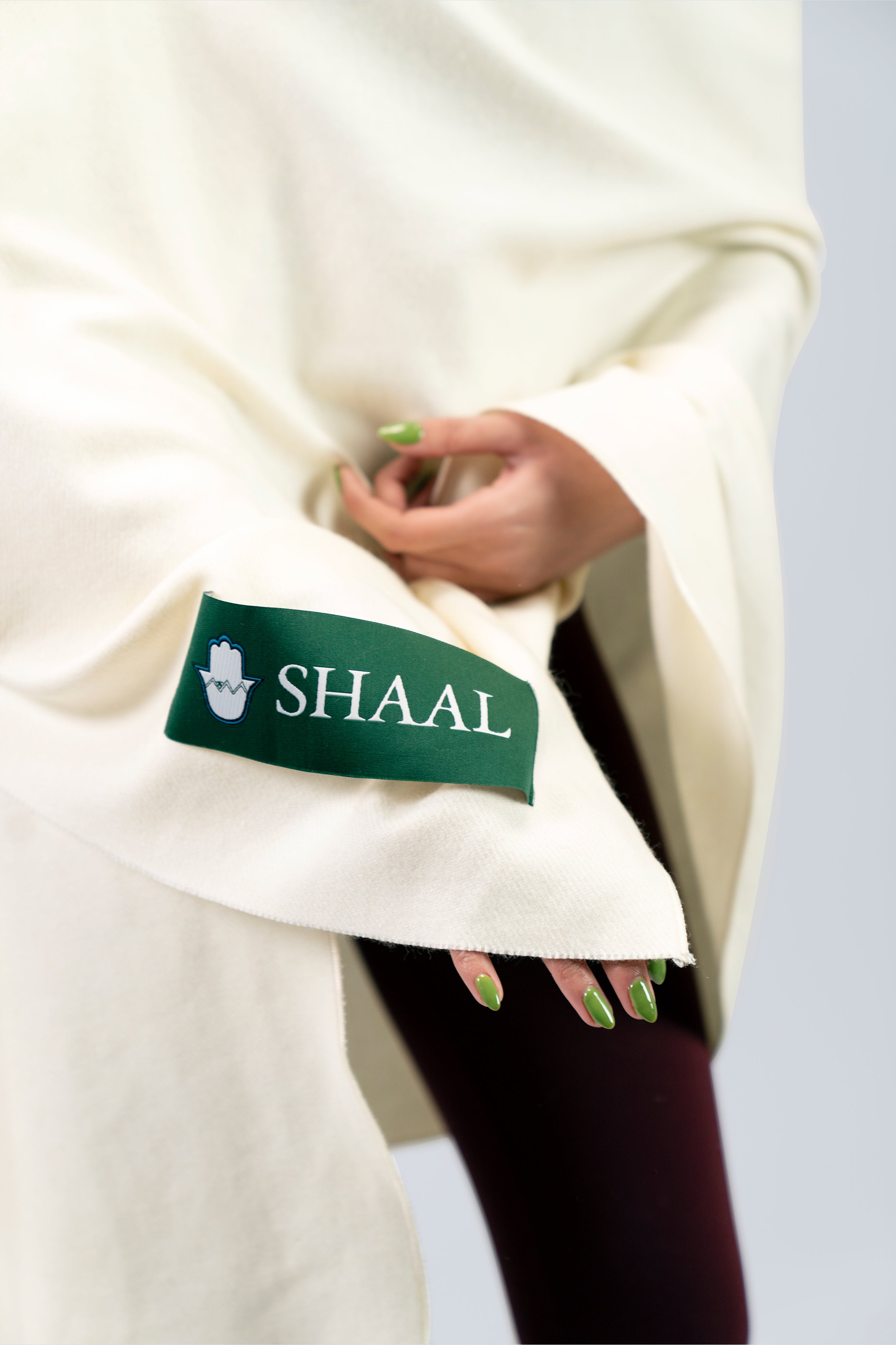 Off-white heavyweight lamb wool shawl detail of green SHAAL woven label held by model